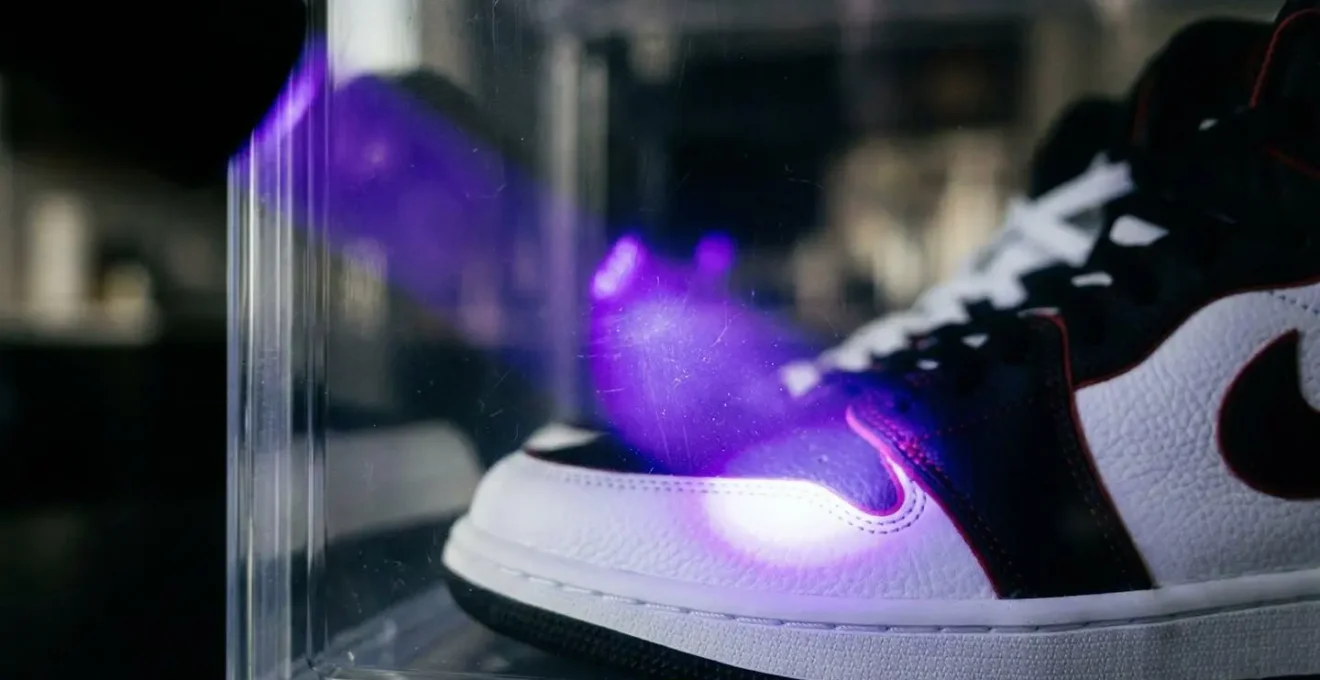 Gros plan sur une main tenant une lampe UV pointée vers une boîte transparente contenant des sneakers, montrant la barrière protectrice